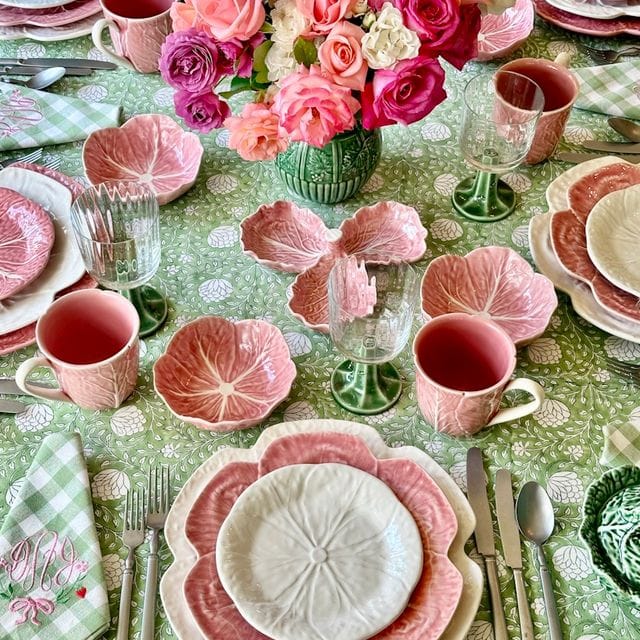 Decorative table setting with pink cabbage plates, cups, and a centerpiece on a green patterned tablecloth.