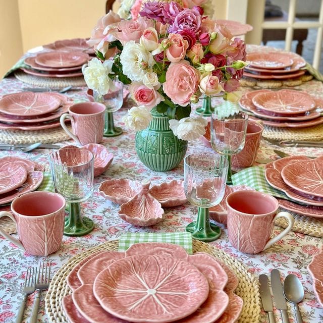 Dining table set with pink ceramic plates, cups, and floral centerpieces.