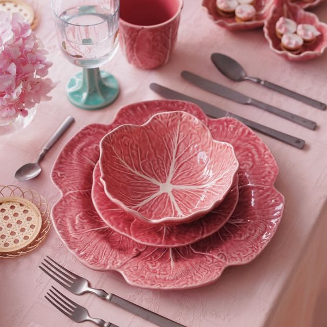 Pink ceramic cabbage leaf-patterned dishes on a table with silverware and glasses.