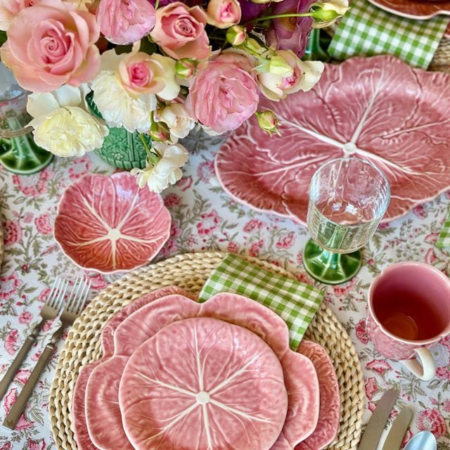 Decorative table setting with pink cabbage plates, flowers, and cutlery on a patterned tablecloth.