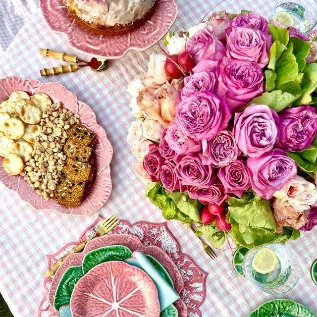 Table setting with pink floral arrangement, plates with food, and decorative items on a checkered tablecloth.
