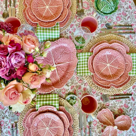 Decorative table setting with floral plates, flowers, and cutlery on a patterned tablecloth.