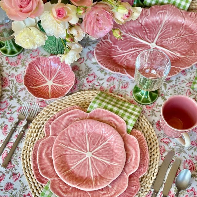 Decorative table setting with pink cabbage leaf plates, flowers, and cutlery on a patterned tablecloth.