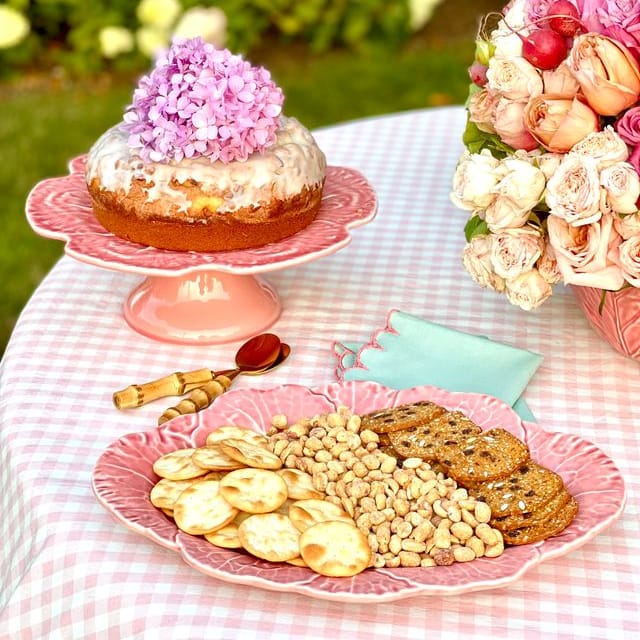 Table with cookies, crackers, and a cake on a checkered tablecloth outdoors.