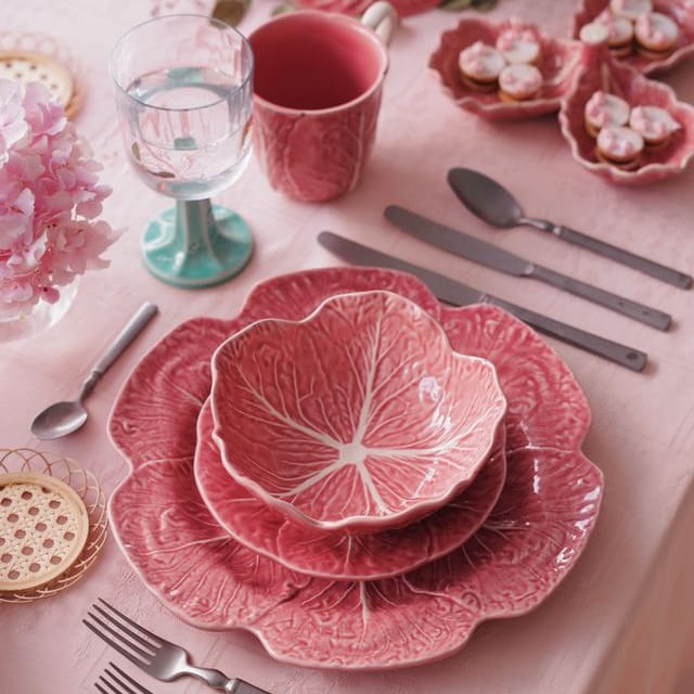 Pink ceramic cabbage leaf-patterned dishes on a table with silverware and glasses.