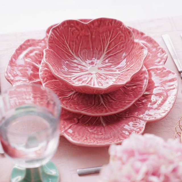Set of pink ceramic plates with cabbage leaf patterns on a light pink tablecloth.