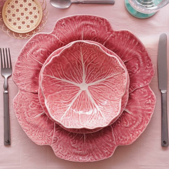 Pink cabbage leaf-patterned plates on a pink tablecloth with silverware and glasses.