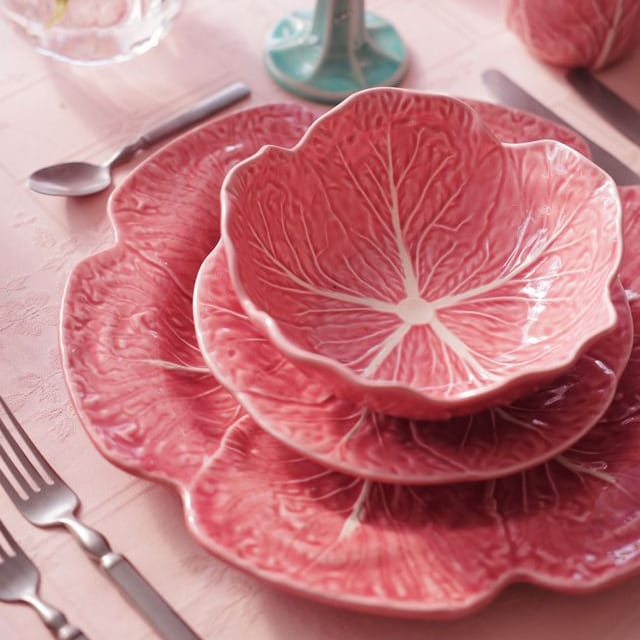 Pink cabbage leaf-patterned dinnerware set on a table with floral decorations.