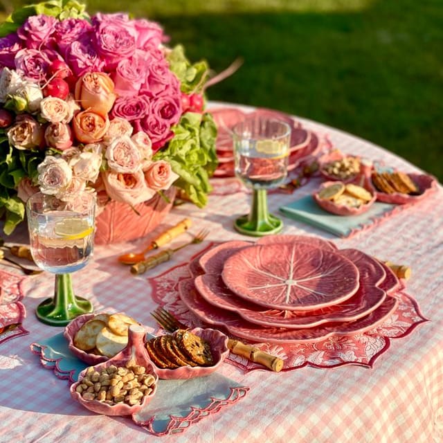 Outdoor table setting with pink floral centerpiece, plates, and glasses on a grassy background