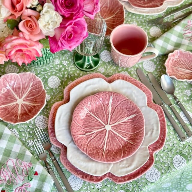 Decorative table setting with pink floral arrangement, plates, and cutlery on a checkered tablecloth.