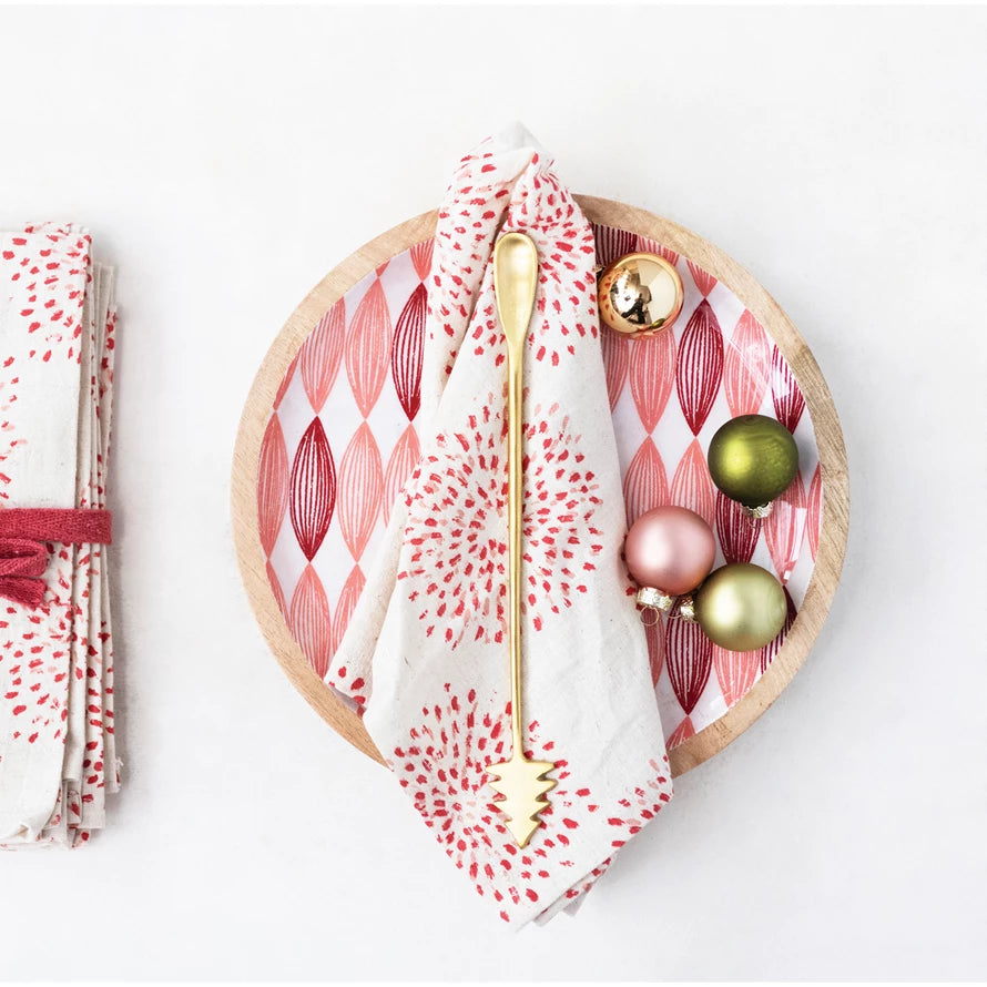 A 9-inch brass cocktail spoon with a Christmas tree handle, displayed on a decorative napkin next to holiday ornaments.