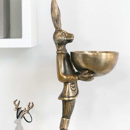 A brass-gold finished metal stand in the shape of a rabbit holding a bowl.