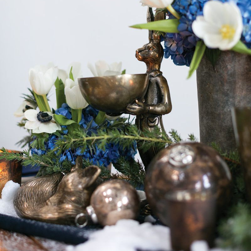 A brass-gold finished metal stand in the shape of a rabbit holding a bowl.