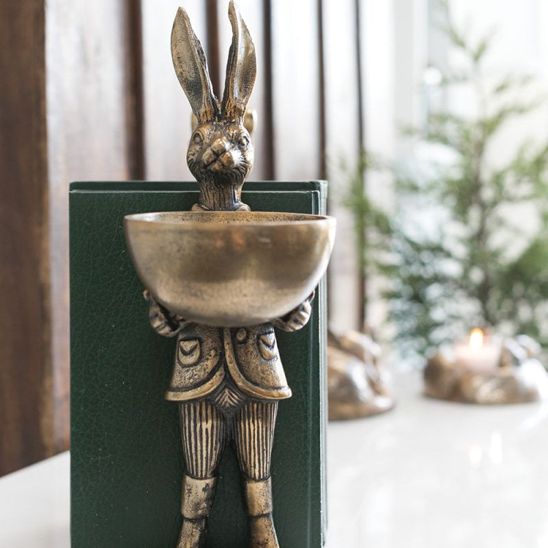 A brass-gold finished metal stand in the shape of a rabbit holding a bowl.