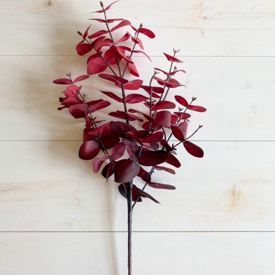Artificial red eucalyptus branch on a light wooden background