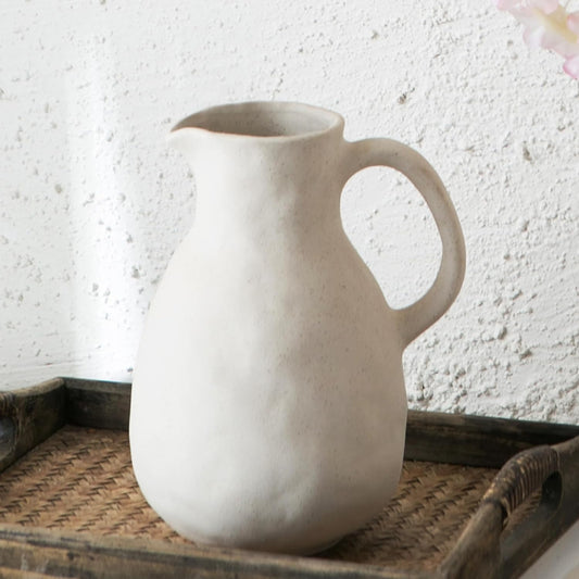 A beige ceramic vase with a rustic texture, resembling a kettle, placed on a wooden surface.