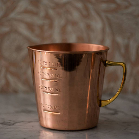 Copper measuring cup with gold handle on a textured surface