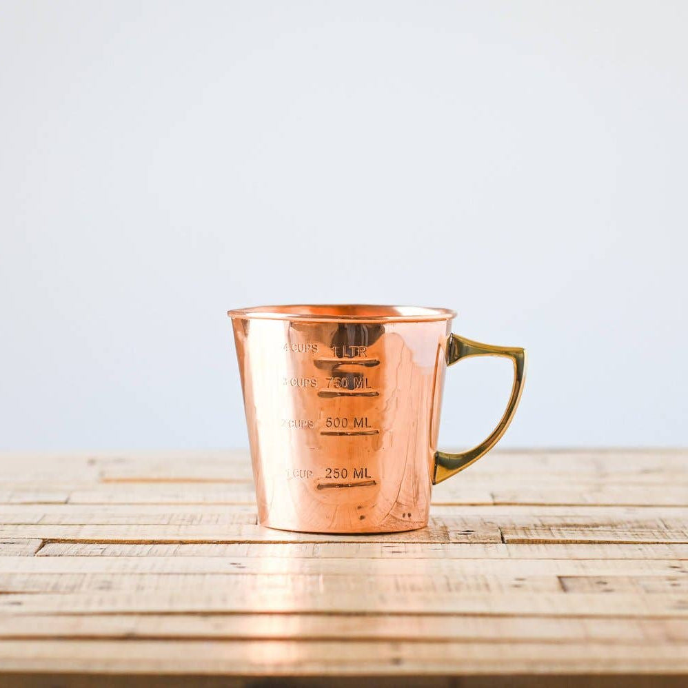 Copper measuring cup on a wooden surface with a light blue background