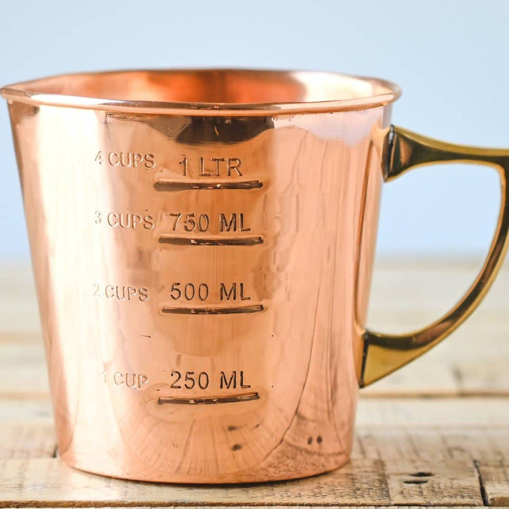 Copper measuring cup with volume markings on a wooden surface