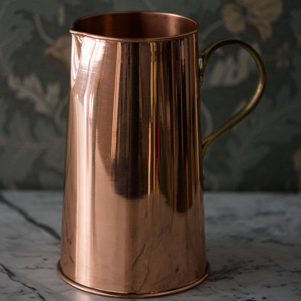 Copper pitcher on a marble surface with a floral-patterned curtain in the background