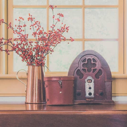 Vintage radio with a copper vase of red berries on a wooden surface