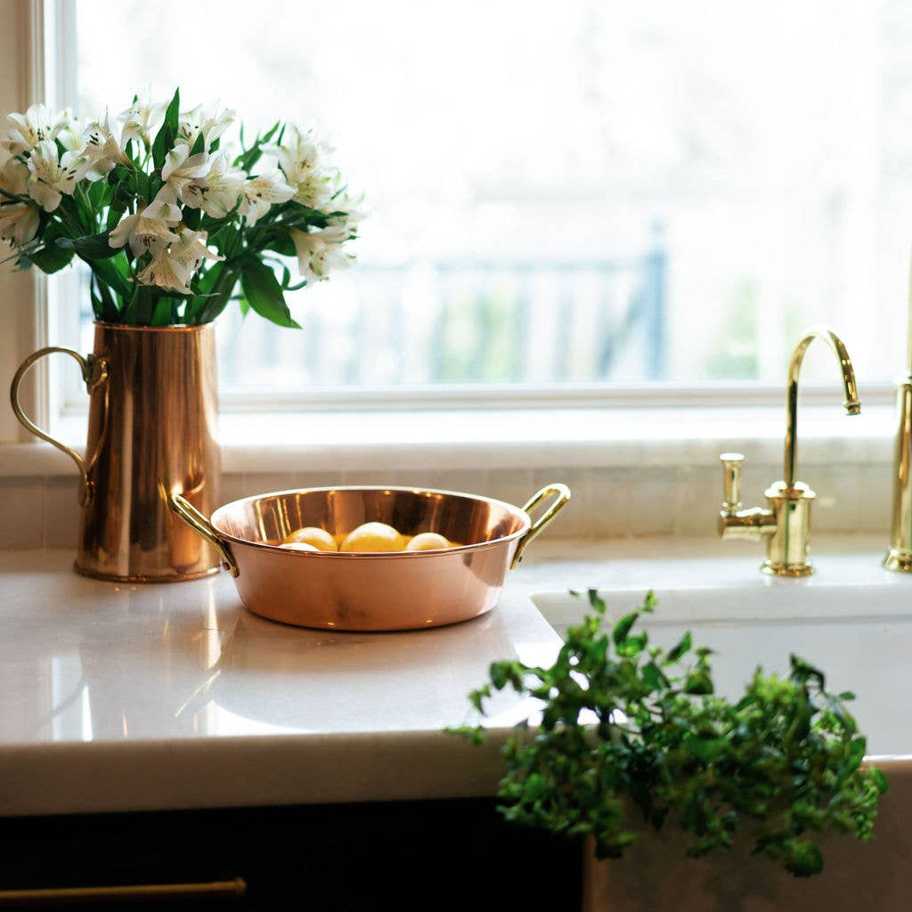 Copper pitcher and bowl on a kitchen counter with flowers and a plant.