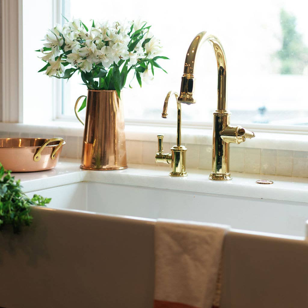 Kitchen sink with gold faucet, copper pitcher, and white flowers.