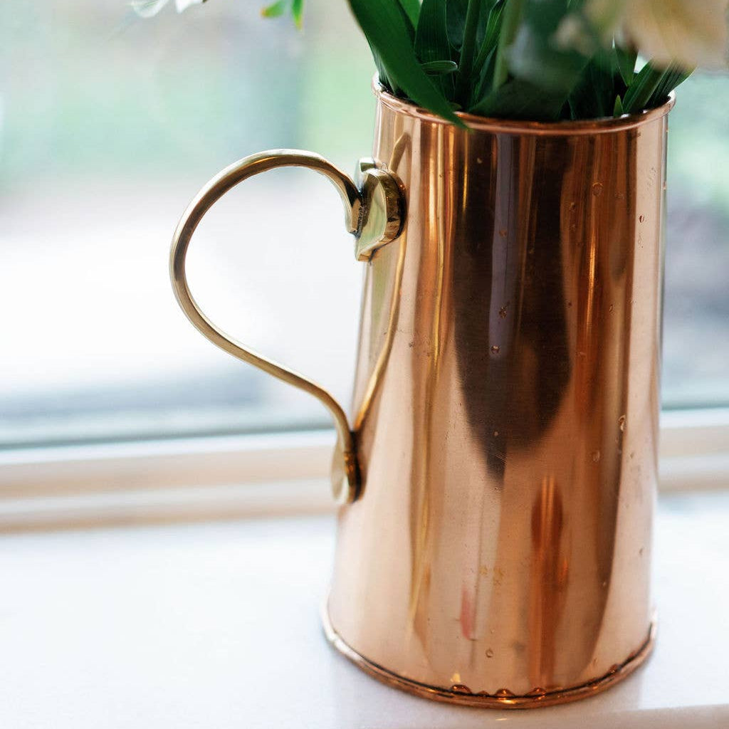 Copper pitcher with flowers on a windowsill