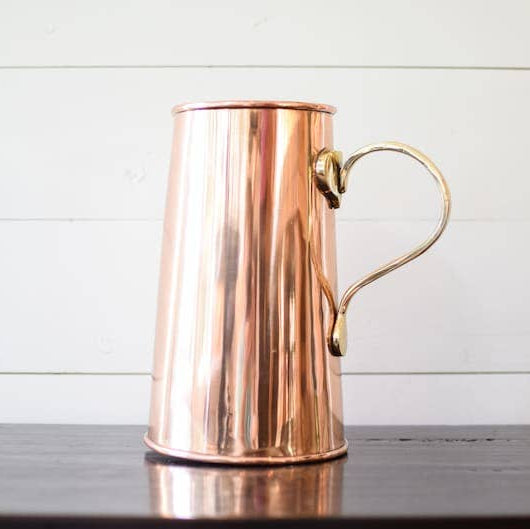 Copper pitcher with a handle on a wooden surface and white wooden panel background