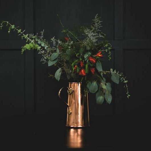 Copper pitcher with greenery against a dark background