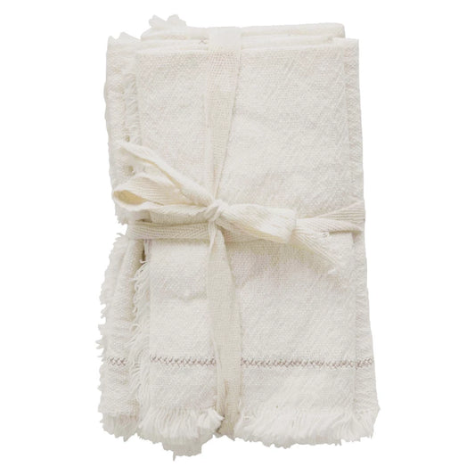A set of four folded white cotton napkins with decorative fringe, tied together with a string.