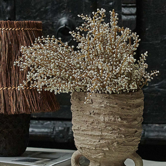 An arrangement of artificial heather in a cream color, displayed in a beige vase on a table.