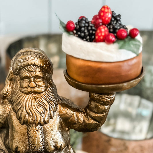 A faux fruit tart arranged on top of a figure resembling Santa Claus holding a tray.
