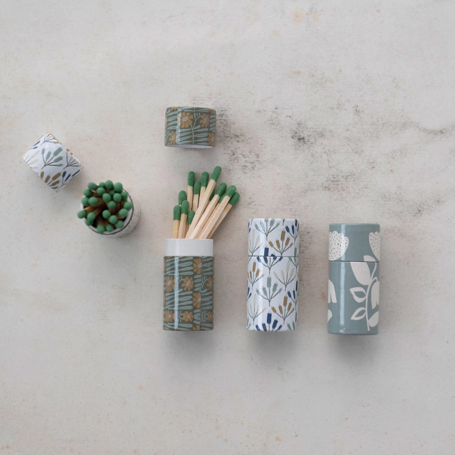 Three cylindrical tube matchboxes, each with a different floral pattern design.