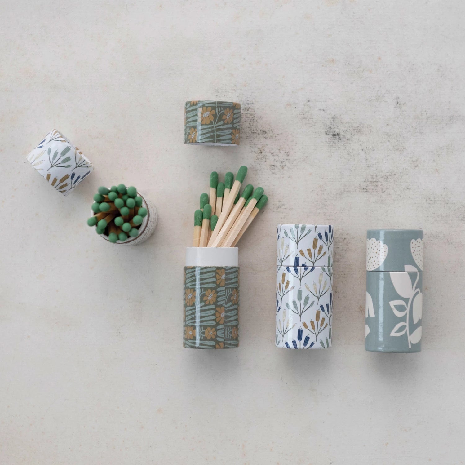 Three cylindrical tube matchboxes, each with a different floral pattern design.