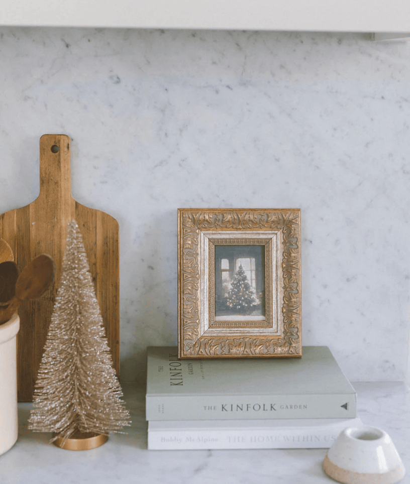 Decorative Christmas tree and framed photo on books against a textured wall.