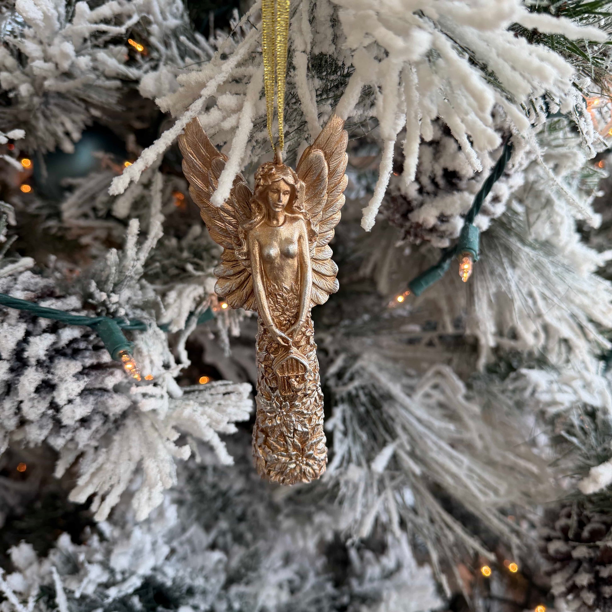 Decorative angel ornament hanging on a frosted Christmas tree with lights.