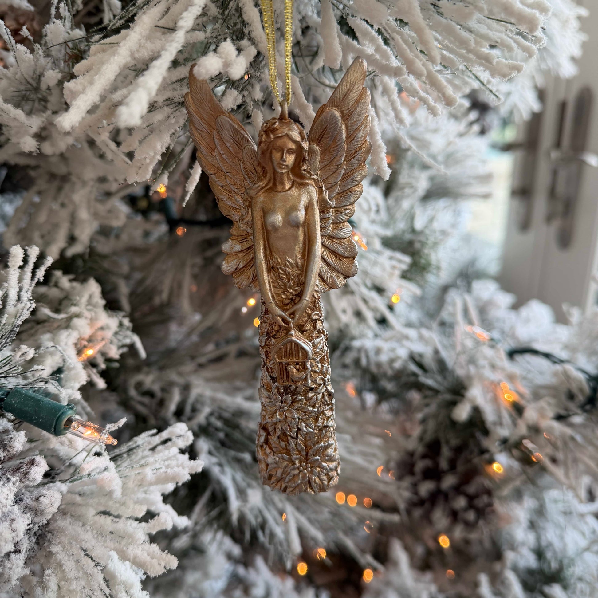 Decorative angel ornament hanging on a frosted Christmas tree.