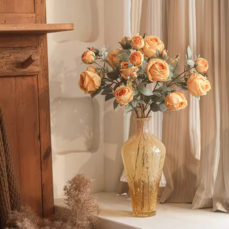 Vase with orange flowers on a surface next to a wooden cabinet.