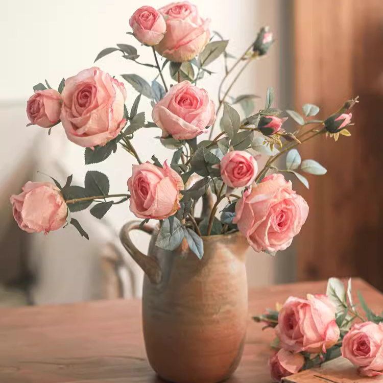 Pink roses in a ceramic vase on a wooden surface with a blurred background