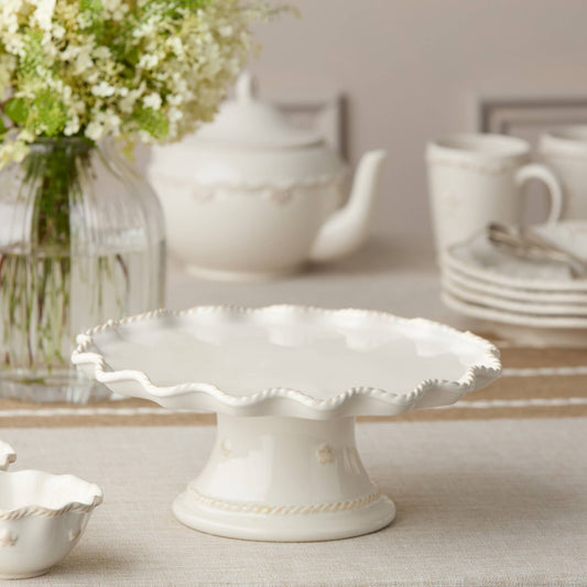 11.5" White ceramic cake stand on a table with floral arrangement and teacup in the background Ruffled Shape