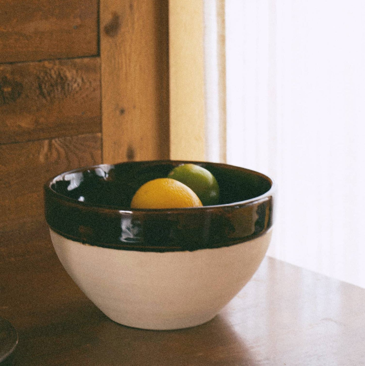 White bowl with brown rim containing fruits on a wooden surface