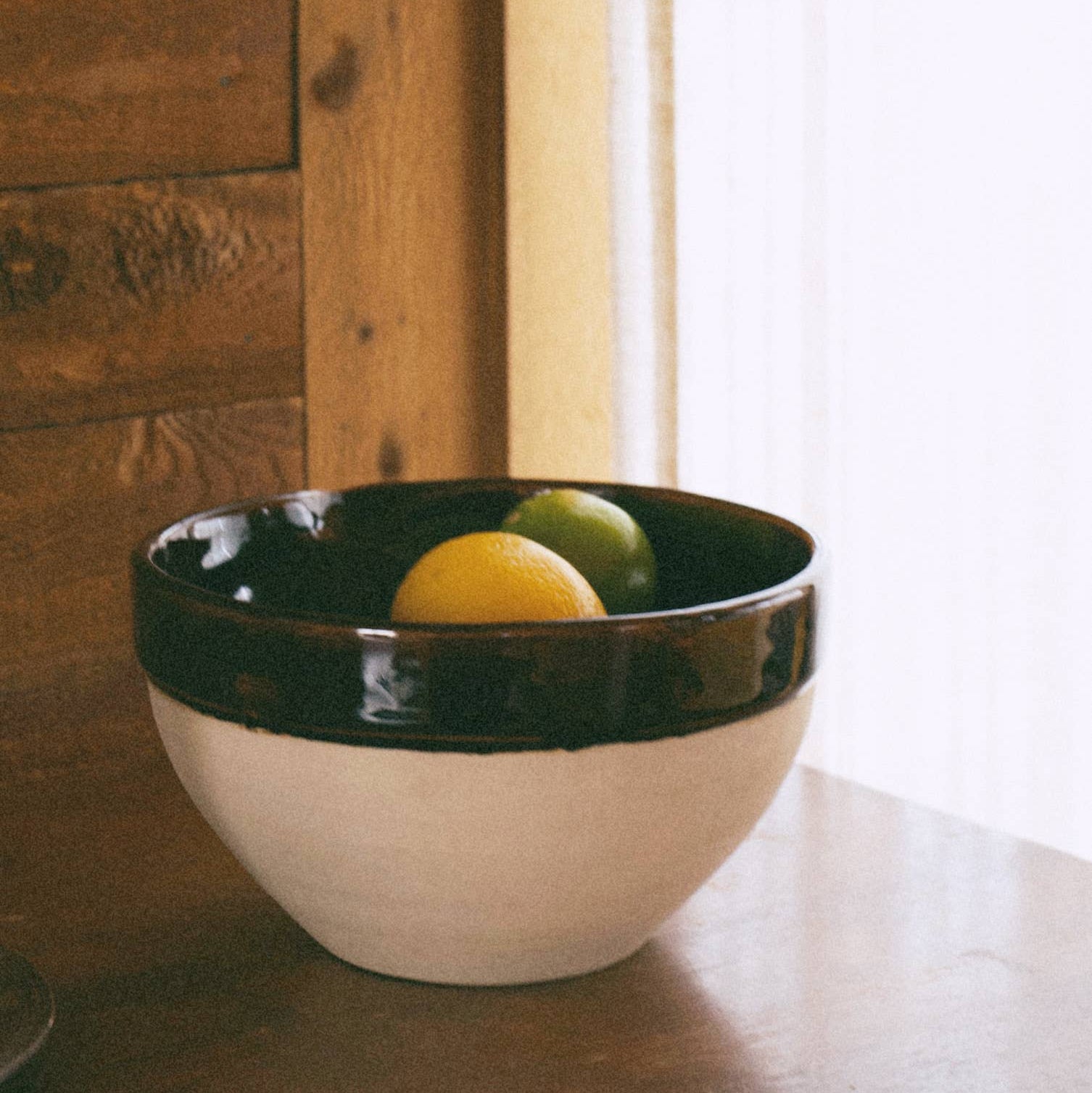 White bowl with brown rim containing fruits on a wooden surface