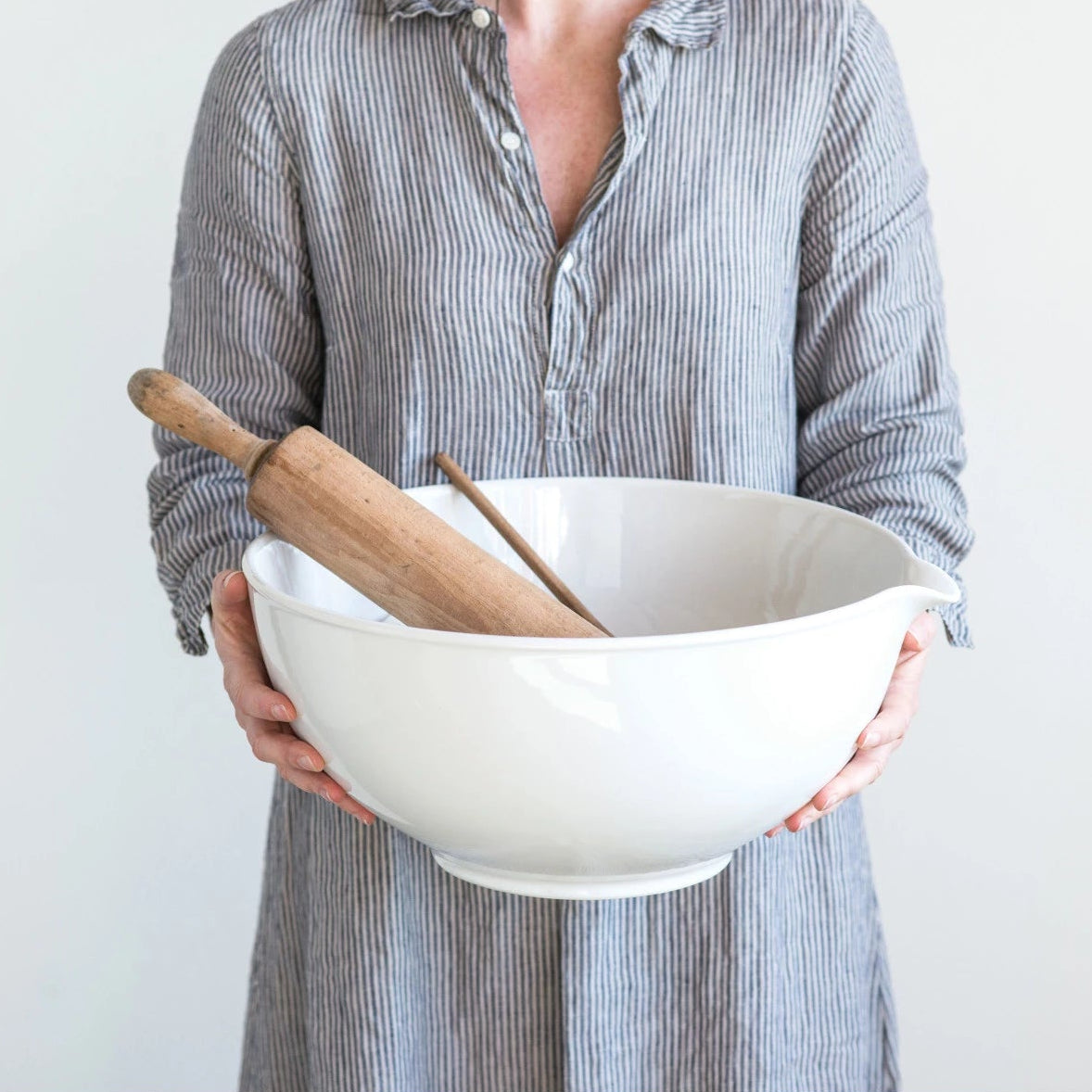 Person holding a white bowl and wooden rolling pin against a plain background