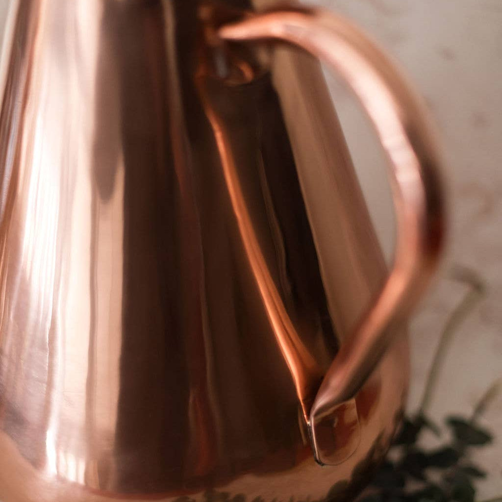 Copper pitcher on a textured surface with greenery