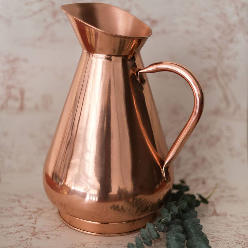 Copper pitcher on a textured surface with a plant