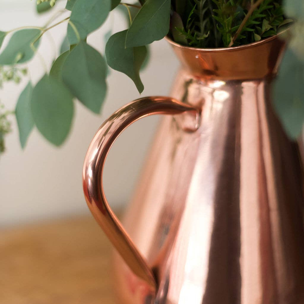 Copper pitcher filled with greenery on a wooden surface
