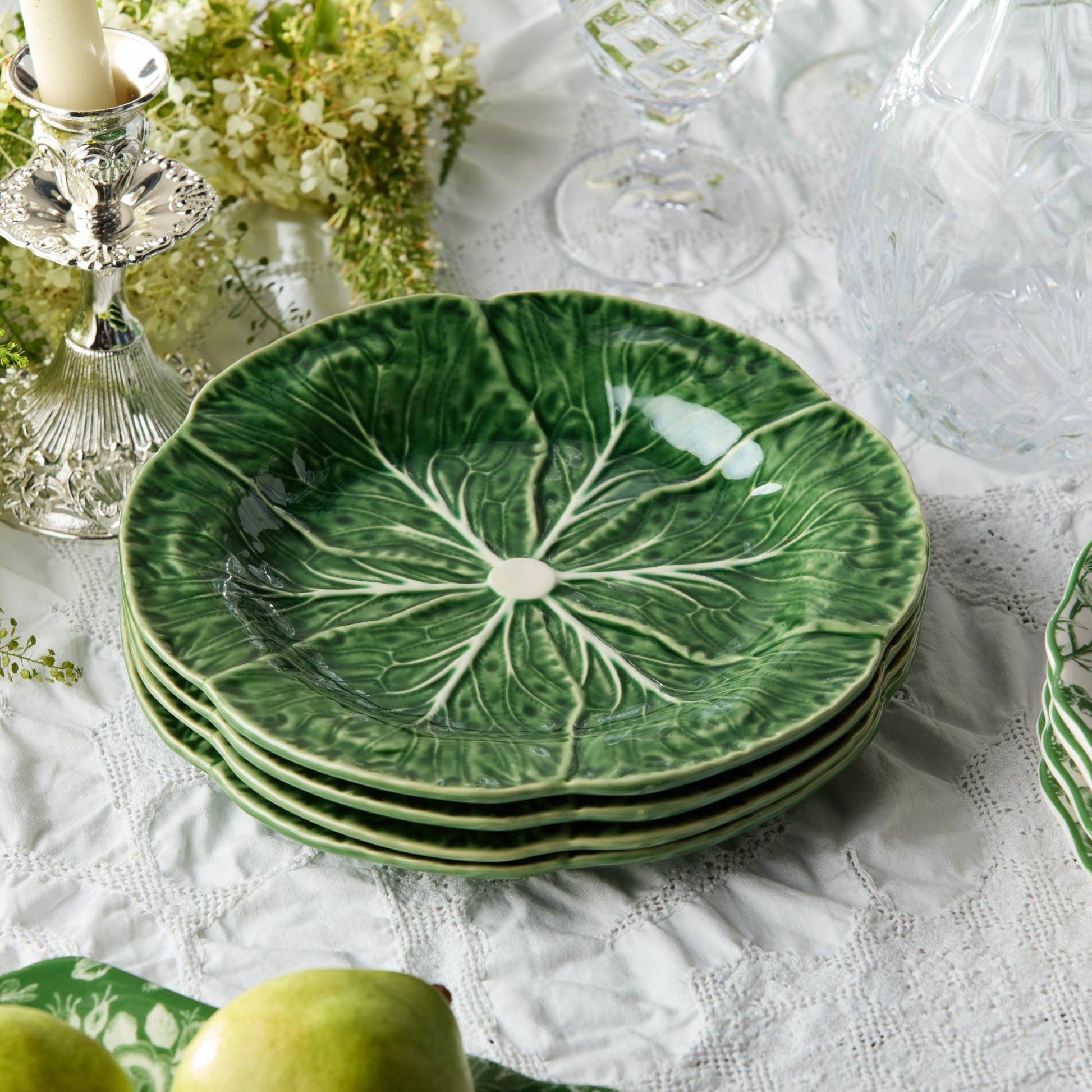 Stack of green cabbage 9" ceramic plates with leaf design on a white lace tablecloth.