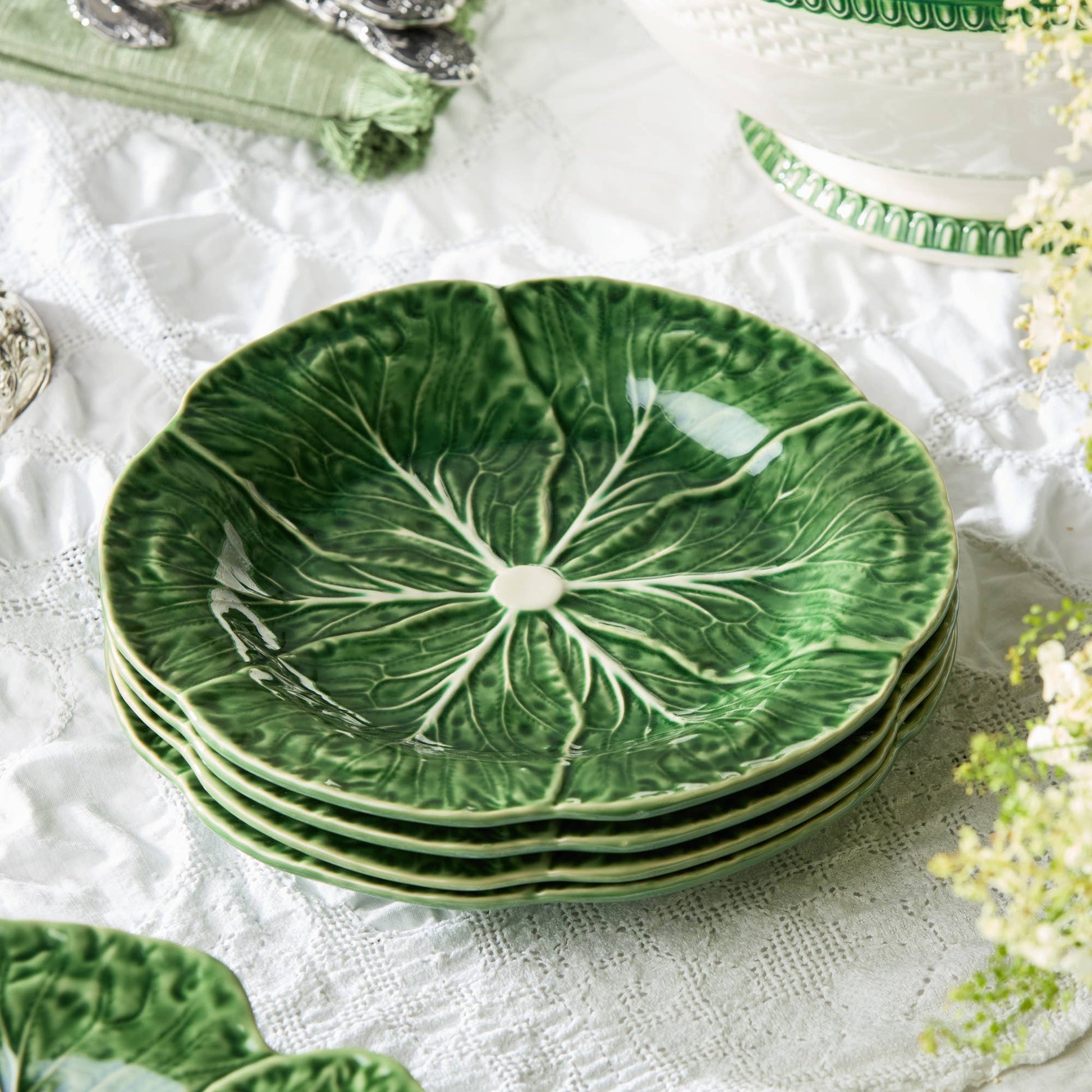 Set of green ceramic plates with leaf design on a white lace tablecloth.