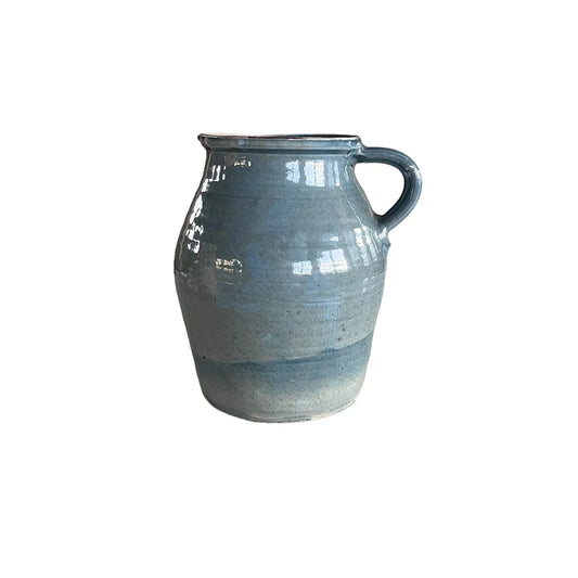 A tall, round, blue ceramic jug designed as a vase, with a handle on the side and a subtle speckled pattern.